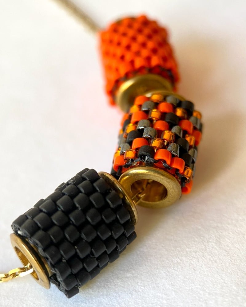 Vergoldete Halloween-Halskette mit drei Miyuki-Perlencharms in Schwarz, Orange und einem schwarz-orangefarbenen Muster mit goldfarbenen Akzenten auf einer Schmuckbüste - Fleur du Jour